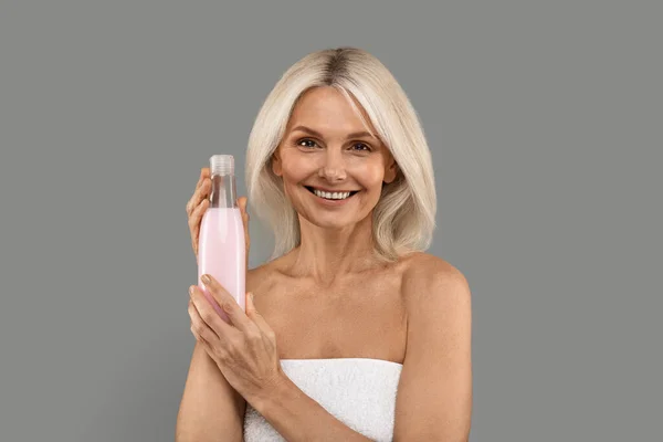 美丽的微笑成熟的女人沉浸在牙龈广告新化妆品中 快乐迷人的老太太站在免费工作室的背景 复制空间上 拿着美容品瓶 — 图库照片