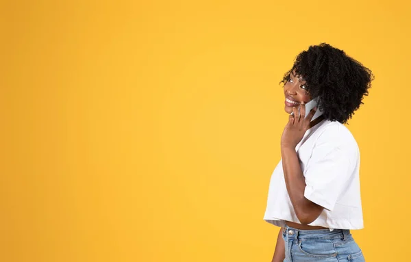 快乐的年轻黑人卷曲女士穿着白色T恤打电话 看着复制的空间 孤立在橙色的背景下 工作室 好消息 广告和提供 销售更新 生活方式 — 图库照片