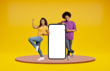 Duygusal mutlu siyah milenyumlar, beyaz ekranlı büyük bir telefonla poz veren sıradan bir adam ve kadın, mesaj veya reklam için boş alan, online kumar oynayan siyahi insanlar, nakit para kazanıyorlar.