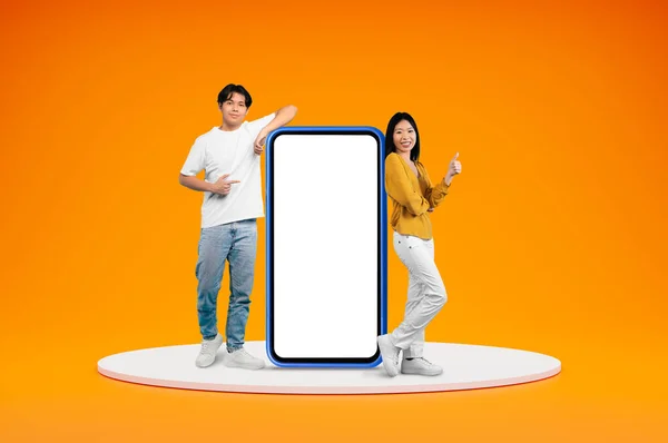 快乐的中国千禧一代男人和女人在平台上摆姿势 拿着白色的空屏风 露出大拇指 在橙色的背景上与世隔绝 空旷的空间 很好的网上报价 — 图库照片