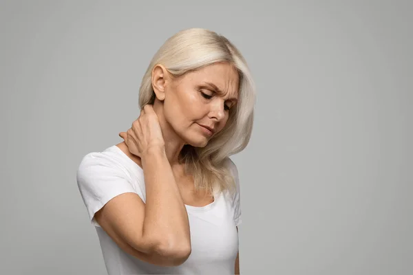 心烦意乱的成熟妇女颈部疼痛 手压老年妇女颈部酸痛 骨质疏松症 站在灰色工作室背景之上 复制空间等特征描述 — 图库照片