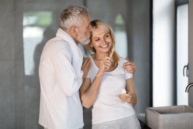 Banyoda dişlerini fırçalayan mutlu bir çift, karısını öpen bir adam, sabah hijyeni yapan romantik yaşlı eşler, evde neşeli erkek ve kadın kaynaşması, uzay kopyası.