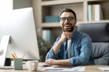 Modern Ceo. Ofiste oturan yakışıklı genç iş adamının portresi, iş yerinde gözlük takan, kameraya bakan ve gülümseyen mutlu genç girişimci,