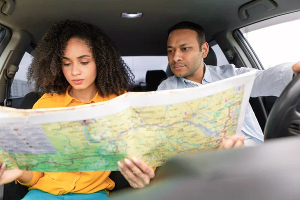 Car Navigation Issues. Confused Middle Eastern Spouses Lost During Travel By Auto, Holding Map Choosing Route, Having Difficulties Navigating their Adventure, Sitting In Automobile Inside