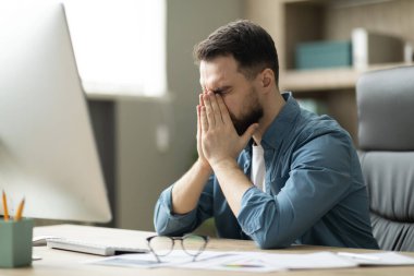 Çalış Burnout. Ofiste oturan yorgun genç işadamı, yorgun erkek girişimci gözlerini ovuşturuyor, aşırı çalışan erkek yorgunluğu ve bilgisayar başında çalıştıktan sonra göz yorgunluğu çekiyor.