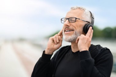 Egzersiz için güzel müzik. Gözlüklü, gözlüklü, kablosuz kulaklıklarına dokunan, kapalı gözlerle gülümseyen, favori şarkıları dinleyen, açık havada egzersiz yapan sporcu.