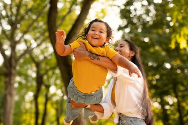 Oyun zamanı Joy. Neşeli Asyalı Anne, Heyecanlı Kızını Kaldırır ve Sürer, Yazlık Parkı 'nda Eğlenceli Açık Hava Maceraları Yapıyor. Anne ve çocuk kaynaşıyor ve dışarıda eğleniyorlar.