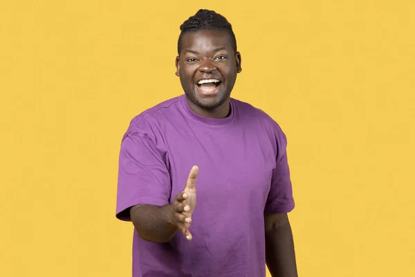 问候的概念 微笑的非裔美国人伸出他的手在黄色工作室背景上握手 穿紫色T恤的正人君子达成协议或交易 提供伴侣关系 — 图库照片