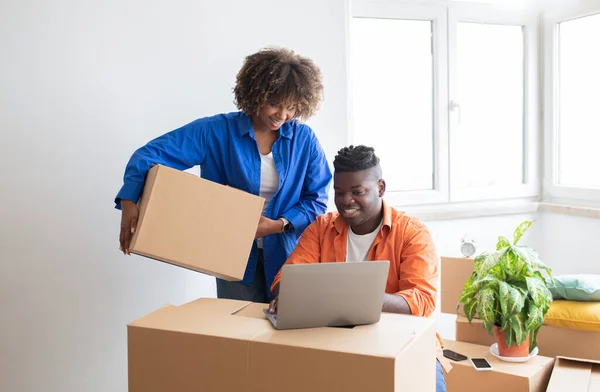 Great Website. Happy Black Couple Using Laptop While Moving Home, Smiling African American Spouses Checking Relocating Companies In Internet, Sitting Among Cardboard Boxes In Flat, Copy Space