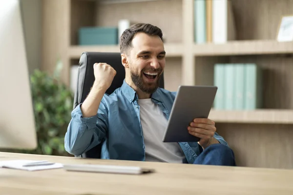 快乐的年轻商人 带着数码平板电脑庆祝办公室的成功 坐在工作场所 千禧年的男性企业家握手大喊 对网上的胜利做出情绪反应 — 图库照片