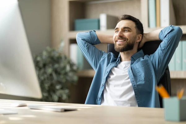 Portrait Of Smiling Millennial Male Entrepreneur Relaxing At Workplace In Office, Happy Young Businessman Leaning Back In Chair With Hands Behind Head, Resting At Desk After Working On Computer