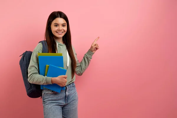 提供教育 带着背包的漂亮女学生和指点粉红背景广告免费位置的工作簿 在复印空间边微笑着少女的藏书和指点 — 图库照片