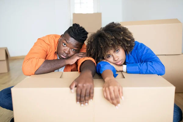 Upset Black Spouses Leaning At Cardboard Box, Having Stress While Moving To Their New Home, Exhausted African American Couple Suffering Problems During Relocation, Feeling Tired And Depressed