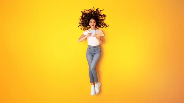 stock image Mobile Offer. Happy Young Woman Using Cell Phone, Scrolling Online News And Browsing Internet, Texting Via New Smartphone Lying On Yellow Studio Background. Panorama, View From Above