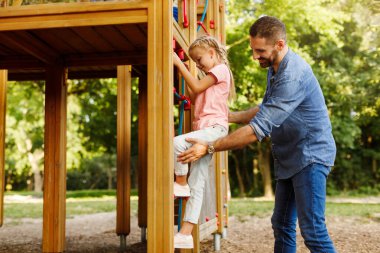 Kızına yardım eden babayla ilgilenmek. Bu arada kız dağlara tırmanıyor. Güneşli bir günde parkta oyun oynuyor ve eğleniyor. Çocuk konsepti için açık hava eğlencesi