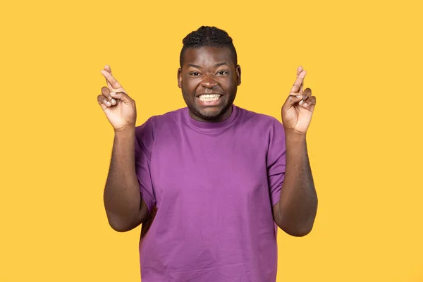 许下美好的愿望年轻快乐的黑人男人站在黄色工作室的背景上 微笑着对着镜头 交叉着手指祈求好运 快乐的人做手指交叉动作 — 图库照片