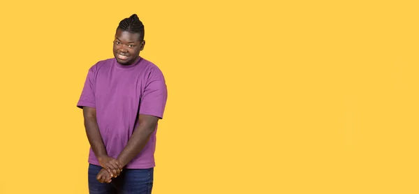 羞怯的概念 黑人装出腼腆的样子 穿着休闲的紫色T恤 站在黄色的工作室背景上 对着相机微笑 有空白的文字空间 — 图库照片