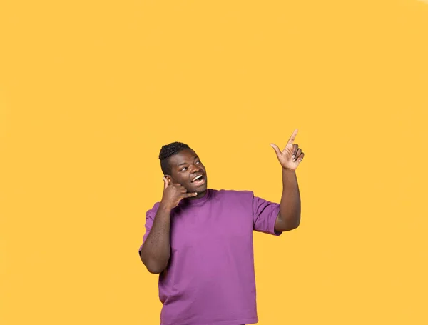 叫我Gesture 快乐的非裔美国人手牵着手 像手机一样靠近耳朵 指向站在黄色工作室背景之上的自由空间 流动通讯概念 — 图库照片