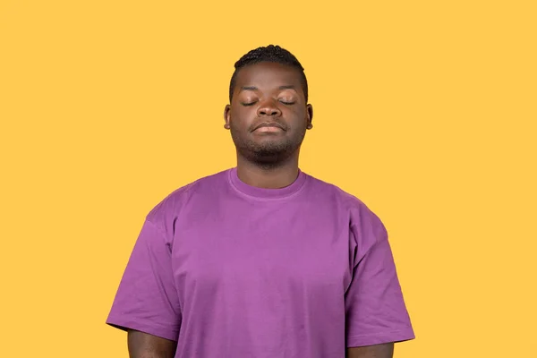 疲惫的黑人摆出困倦的样子 眼睛紧闭在黄色的背景上 表现出疲倦和缺乏激情 穿着紫色的T恤 工作室肖像画 负面情绪 — 图库照片