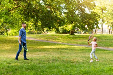 Aile eğlencesi. Babamın kızıyla badminton oynarken, raket tutarken ve büyük bir pipi kullanırken, yaz günü dışarıda parkta vakit geçirirken.