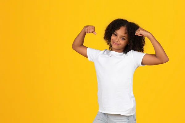 티셔츠에 긍정적 소녀는 노란색 스튜디오에서 근육을 보여줍니다 훌륭한 스포츠 라이프 — 스톡 사진