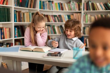 Okul çocukları kütüphanede oturuyor, kitap okuyor ve ödevlerini yapıyor, sohbet ediyor ya da okul projesini derslere hazırlıyorlar. İlköğretim