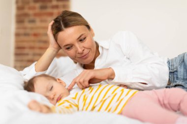 Sevgi dolu bir anne, uyuyan kızına dokunuyor. Yatak odasında uzanıyor, evde hassas anların tadını çıkarıyor. Annelik yaşam tarzı, gündüz uykusu rutin konsepti.