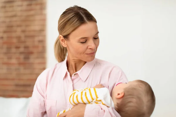 stock image Mothers care. Loving mom holding her little sleeping baby daughter on hands and lulling her kid, sitting on bed at home. Mommy caring for her infant girl while she sleeping peacefully