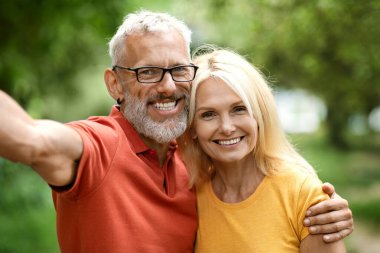 Mutlu olgun eşler, dışarıda selfie çekerken neşeli yaşlı çiftlerin kucaklaşmalarını ve kameraya poz vermelerini ve emeklilik hayatlarının tadını çıkarmalarını çekiyorlar.