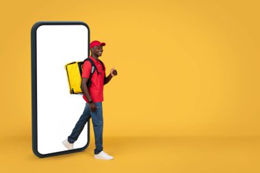 Kocaman bir sırt çantalı, turuncu arka planda izole bir şekilde boş ekranlı akıllı telefondan çıkan üniformalı Afro-Amerikan teslimatçı. Web sitesi, dağıtım servisi, tavsiye uygulaması
