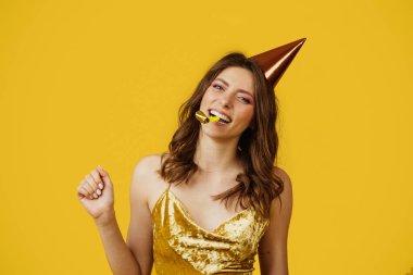 Zarif elbiseli ve doğum günü şapkalı muhteşem bayan sarı stüdyo arka planında bayramı kutluyor. Mutlu kadın parti veriyor. Kutlama konsepti