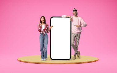 Güzel uygulama. Mutlu Çoklu Etnik Çift Pembe Arkaplan Üzerinde Büyük Boş Akıllı Telefon, Neşeli Genç Arap Adam ve Asyalı Kadın Yeni Mobil Uygulama veya Çevrimiçi Teklif,