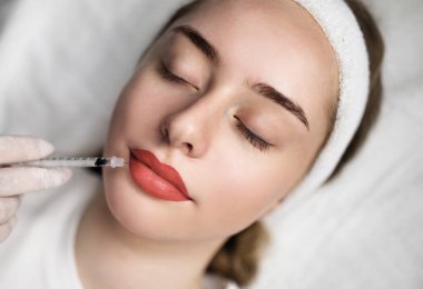 Dudak büyütme. Kozmetolog, güzellik salonundaki estetik tedavide genç kadına Hiyalüronik Asit Enjeksiyonu Yapan Güzellik Uzmanı, Şırıngayı batıran,