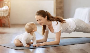 Güzel genç kadın anne evde bebekle yoga yapıyor. Mutlu anne fitness minderinde yatar, küçük tatlı çocukla oturma odasında antrenman yapar. Sağlıklı aile yaşam tarzı kavramı