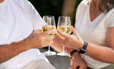 Beyaz tişörtlü yaşlı Avrupalı karı ve koca, şarap kadehleriyle tezahürat yapıyor, yaz tatilinin tadını çıkarıyor, açık havada, kırpılmış. Hafta sonu birlikte, romantik randevu, yıldönümü, yakın çekim.