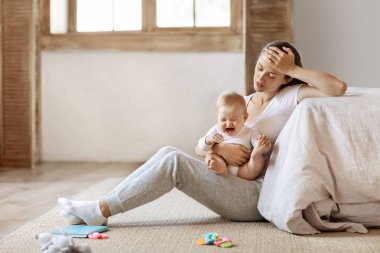 Yorgun bebek annesinin ellerinde ağlıyor. Üzgün, bitkin anne kucağında ağlayan küçük çocukla yerde oturuyor. Yatak odasının içi, fotokopi odası. Doğum sonrası depresyon konsepti