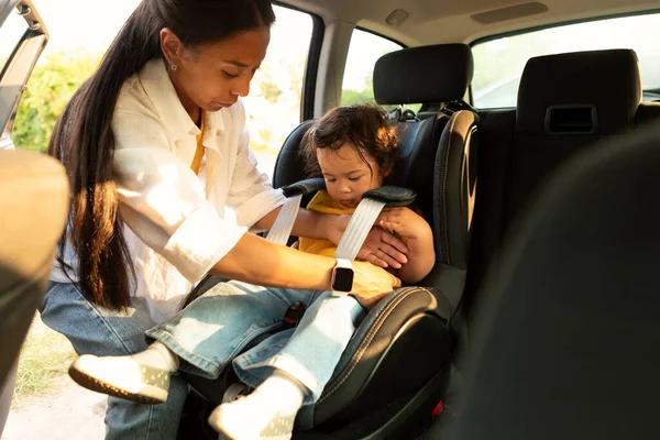 Safe Automobile Ride With Infant. Asian Mom Seating Baby Daughter In Safe Toddler Chair In Car, Adjusting Harness for Little Child Ensuring Secure and Comfortable Auto Journey. Selective Focus
