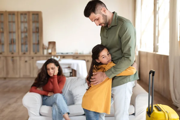 Divorce, Family Separation. Unhappy Kid Girl Hugging Dad While He Leaving Home With Suitcase After Quarrel, Child Suffering From Parents Breakup, Experiencing Problem In Marriage Relationship