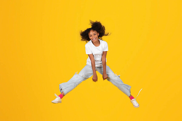 Happy excited adolescent african american girl in white t-shirt jump, freezes in air, has fun, isolated on orange background, studio. Sale, human emotions, lifestyle, study and knowledge, freedom