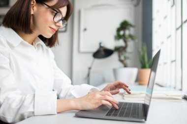 Gözlüklü genç beyaz iş kadını bilgisayarda çalışıyor, ofis içi mesleğinden zevk alıyor, klavyeye odaklanıyor. İş, resmi yaşam tarzı, reklam ve teklif