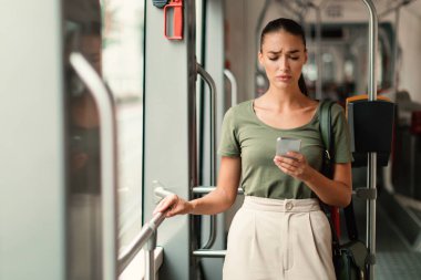 Şehir Mesafesi. Mutsuz Bayan Yolcu cep telefonu mesajları kullanıyor modern tramvayda duruyor şehir ulaşımı hakkında kötü haberler okuyor. Ulaşım Konseptinde İnternet Bağlantısı Sorunu