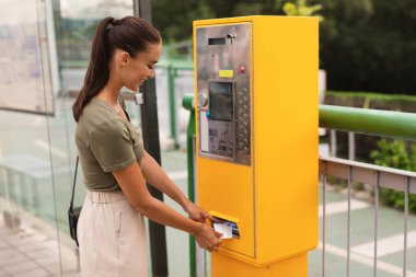 Neşeli Bayan Yolcu Tramvay Turu için ödeme yapıyor ve bilet otomatını açık hava istasyonunda duruyor. Yan Görüntü Görüntüsü. Şehirde Toplu Taşımacılık ile Giden Kadın