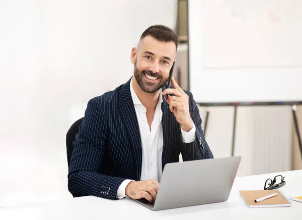 スーツのひげを持つ笑顔の慎重な成熟した男性は テーブルに座って ラップトップを使用し 現代のコワーキングオフィスのインテリアで電話を作ります ビジネスマン ビジネス マネージャー ミーティング コミュニケーション — ストック写真
