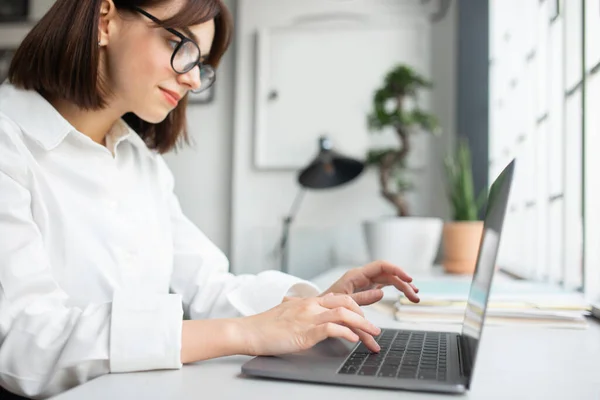 年轻的高加索女商人戴着眼镜在电脑上工作 喜欢在办公室内部从事专业工作 有选择地专注于使用键盘 正式生活方式 广告和提供 — 图库照片
