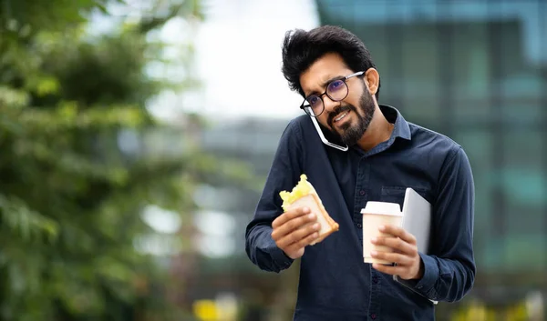 若いインドの起業家は 通りの散歩中に電話で話し テイクアウトコーヒーとサンドイッチを持っています 真剣なビジネスマンは ランチブレイクアウト中にビジネスコールを持っています コピースペース — ストック写真