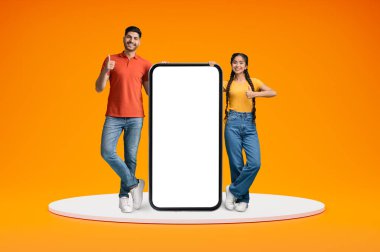 Mutlu Hintli çift, Big Blank Smartphone 'un yanında duruyor ve Başparmak Yukarı, Genç Doğu eşleri, Mobil İlan ya da Teklif İçin Kopya Alanını Gösteriyorlar, Portakal Arkaplan, Kolaj,