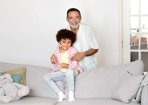 爷爷和孙子邦德 快乐的西班牙裔祖父拥抱和抱抱孙子男孩在家里的沙发上 微笑着对相机 世世代代的家庭联系与爱 — 图库照片