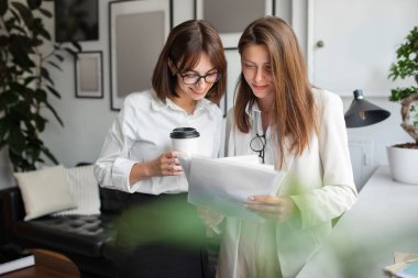 Genç bayan meslektaşlar birlikte başlangıç projesinde çalışıyorlar, bilgileri kontrol ediyorlar, ofiste tartışıyorlar. Şirket çalışanları işbirliği yapıyor, beyin fırtınası yapıyor ve kahve içiyor.