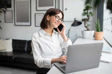 Ofiste otururken cep telefonuyla konuşan rahat bir iş kadını. Gülümseyen bir kadın. Hoş bir cep telefonu sohbeti.