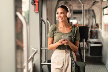 Tramvayda Duran Memnun Yolcu Kadın, Kulaklıkla Telefonla Müzik Dinliyor. Rahat Şehir Taşımacılığı ve Şehir Ulaşım Konsepti